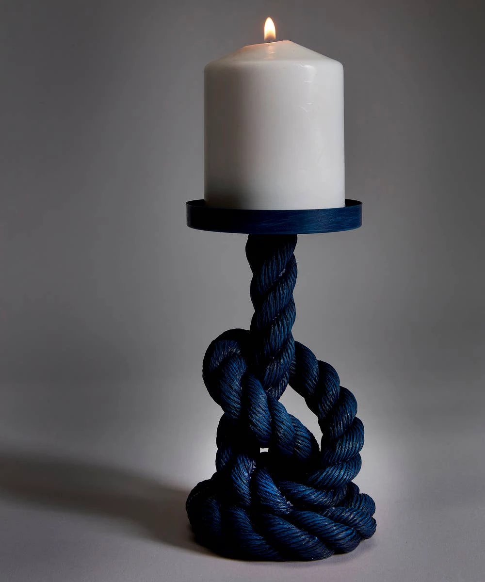White pillar candle atop a thick navy rope pillar, knots form the base, with a circular blue tray around the candle.