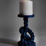 White pillar candle atop a thick navy rope pillar, knots form the base, with a circular blue tray around the candle.