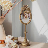 Gold-tone ornate oval pedestal photo frame with floral bow top on a stem and base, holding a vintage portrait.
