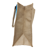 Side view of a tall beige burlap tote with blue lining peeking at the top and a slim strap.