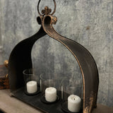 Rustic black cast-iron triple candleholder with three glass cylinders and white pillar candles, arched frame and ring.