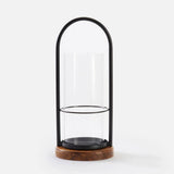 Small iron and wood candle holder: black arched frame around a clear glass hurricane on a round rustic wood base.