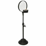 Black iron candlestick stand with circular magnifying glass and a small lit candle tray.