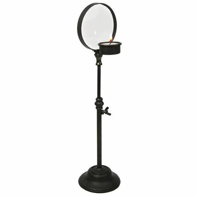 Black iron candlestick stand with circular magnifying glass and a small lit candle tray.