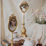 Gold vintage pedestal photo frame with heart-shaped top and oval frame on a tall ornate stand, set on lace and books.