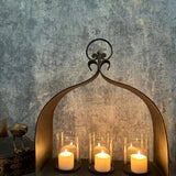 Rustic cast-iron arch candleholder with three glass hurricanes and ivory pillar candles.