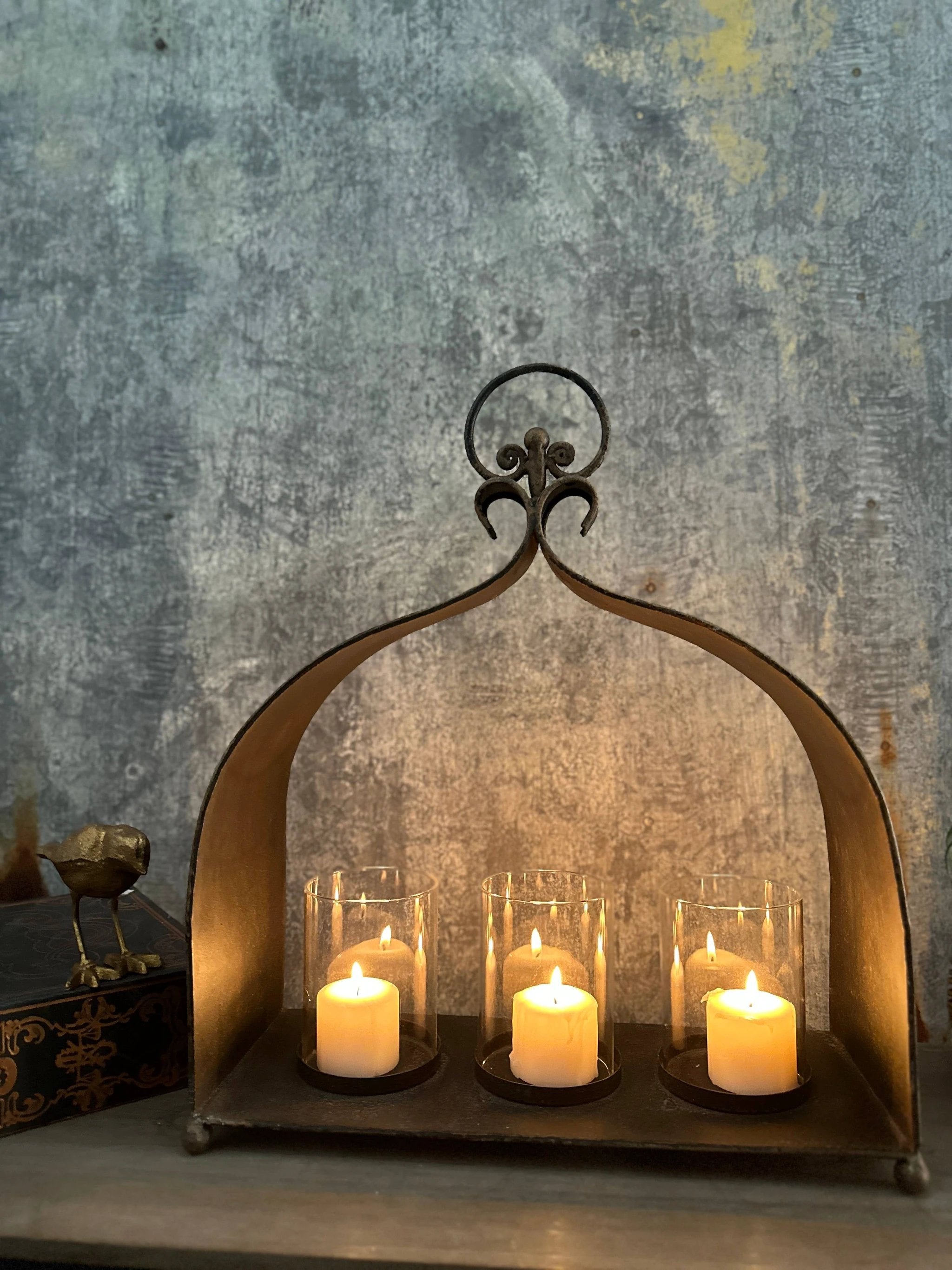 Rustic cast-iron arch candleholder with three glass hurricanes and ivory pillar candles.