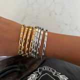Stack of gold- and silver-toned slim bangles with small crystal stones on a wrist.