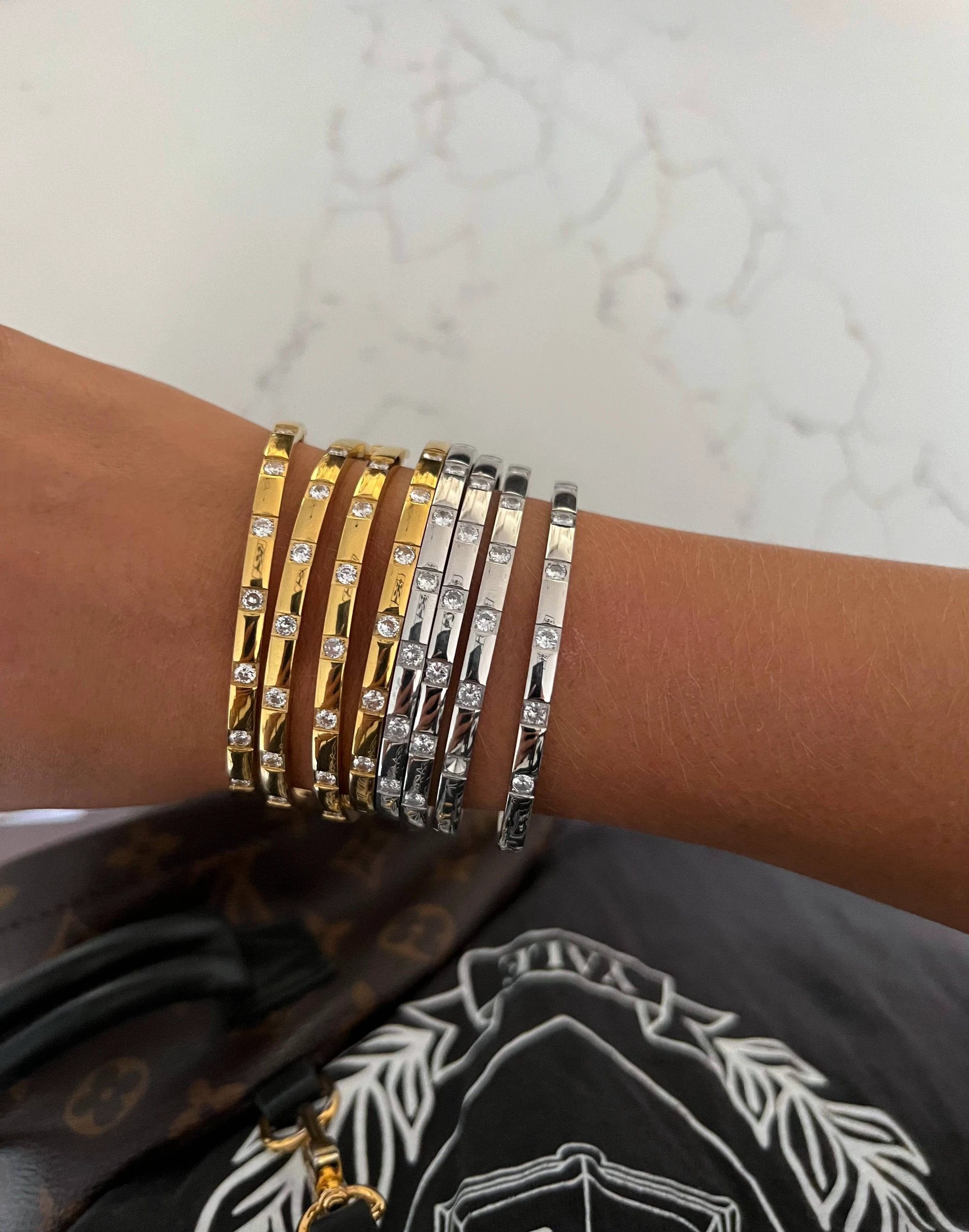 Stack of gold- and silver-toned slim bangles with small crystal stones on a wrist.