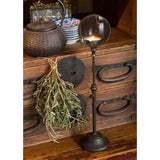 Tall black iron candle holder with a circular magnifying lens at the top; lit candle visible through the lens.